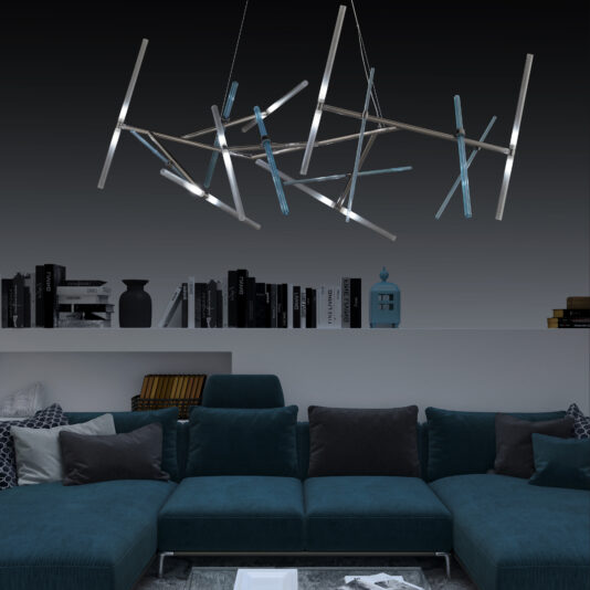 A contemporary living room showcases a large, teal sectional sofa adorned with dark gray and white pillows. Suspended from the ceiling above, the Contemporary Murano Glass Tube Chandelier with intersecting metallic rods illuminates the space. Behind the sofa, a shelf displays an assortment of books, a vase, and various decor items.