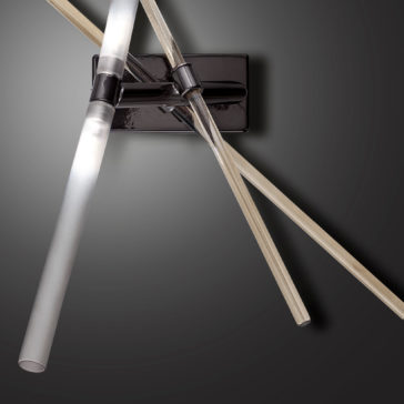 Contemporary Murano Glass Tube Wall Light The Contemporary Murano Glass Tube Wall Light, characterized by its intersecting cylindrical glass tubes, is mounted on a sleek rectangular black base against a smooth grey background. These rods gently emit a soft, diffused light.