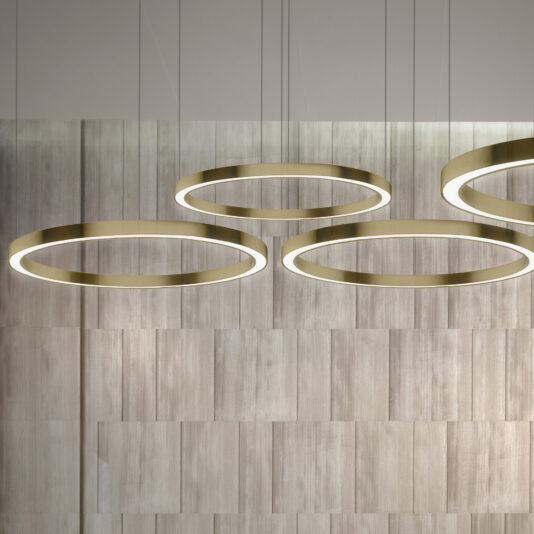 A modern interior showcases the Contemporary Round Downlight Chandelier, featuring three large, circular ring lights suspended from the ceiling. The backdrop consists of vertically arranged wooden panels in various shades of light gray and tan, creating a textured wall effect.