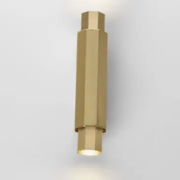 Geometric Satin Gold Tube Style Wall Light A stylish Geometric Satin Gold Tube Style Wall Light with a sleek, cylindrical design is mounted against a plain, light gray background. The fixture emits a soft white light from both ends, creating an elegant and minimalist aesthetic.