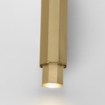Geometric Satin Gold Tube Style Wall Light A close-up image of the Geometric Satin Gold Tube Style Wall Light, showcasing its modern design. The fixture features a hexagonal tube structure with a cylindrical bottom, emitting a soft downward glow. The background is plain and white.