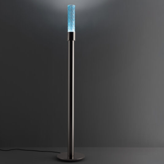 The Modern Faceted Crystal Floor Lamp features a sleek, minimalist design with a cylindrical base and emits a textured, glowing blue light at the top. Set against a plain dark background, this contemporary lamp stands gracefully on its circular base.