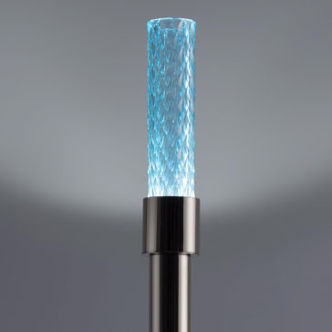Modern Faceted Crystal Floor Lamp The Modern Faceted Crystal Floor Lamp, designed with a slim cylindrical shape and sleek metallic base, features a textured glass tube. The intricately patterned faceted glass is softly illuminated with blue light, enhancing its sophisticated and contemporary appearance against a neutral gray background.