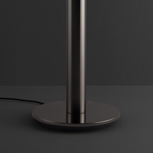 The Modern Faceted Crystal Floor Lamp features a sleek metallic base and a tall, cylindrical stand, showcased against a dark gray background. A black power cord extends from the base's back, while the lighting highlights the smooth and reflective metal surface.