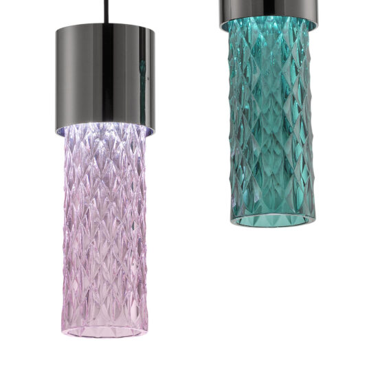 Two Modern Faceted Crystal Pendant Lights with textured glass shades hang from black cords, emitting a soft glow against the white background. The left light features a pink hue, while the right light showcases a teal hue. Both lights are topped with solid, glossy black cylindrical tops.
