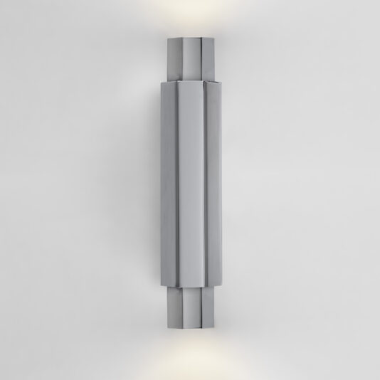 The Modern Geometric Tube Style Wall Light, with its sleek, rectangular design, is mounted vertically on a plain white wall. The light fixture emits soft illumination from both the top and bottom, enhancing the minimalist, contemporary aesthetic.