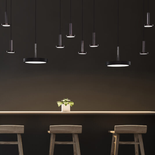 Contemporary Round Pendant Light A minimalist modern cafe interior features a long wooden counter, three wooden high chairs, and a small potted plant on the counter. Several Contemporary Round Pendant Lights hang from the ceiling against a dark wall background, adding to the chic ambiance.
