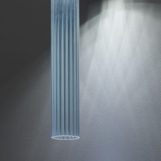 Contemporary Vertical Glass Tube Wall Light A close-up shot of the Contemporary Vertical Glass Tube Wall Light, softly illuminating the textured wall behind it. The fixture features linear detailing and emits a cool-toned glow.