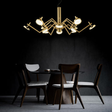 Statement Contemporary Chandelier A modern dining room features a round table with a wooden base and four chairs with white cushions. Above the table hangs the Statement Contemporary Chandelier, a gold, spider-like fixture with multiple arms holding round lights, set against a dark, minimalist background.