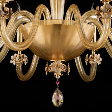 8 Arm Hand Blown Glass Chandelier With Flowers A close-up view of the 8 Arm Hand Blown Glass Chandelier With Flowers showcases its elegance, featuring a golden centerpiece. The design includes intricate curved glass arms adorned with floral embellishments and a teardrop-shaped crystal hanging from the bottom. A black backdrop highlights the chandelier's exquisite details.