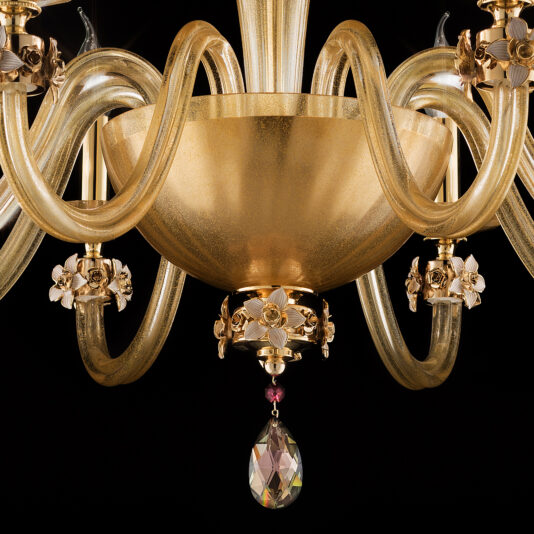 A close-up view of the 8 Arm Hand Blown Glass Chandelier With Flowers showcases its elegance, featuring a golden centerpiece. The design includes intricate curved glass arms adorned with floral embellishments and a teardrop-shaped crystal hanging from the bottom. A black backdrop highlights the chandelier's exquisite details.