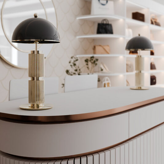 A modern interior features a sleek reception counter with gold and black dome lamps, a round mirror on a patterned wall, and white shelves displaying handbags and accessories. The Black Mid Century Style Table Lamp enhances the space's elegance, seamlessly blending contemporary and luxurious elements.