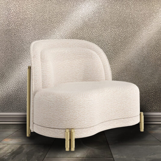 A Contemporary Curved Velvet Armchair, featuring a plush white finish with gold metal accents and short cylindrical legs, is placed in front of a textured taupe-colored wall. The modern chair boasts a rounded back and simple, elegant design. It rests on a tiled floor adorned with a mix of dark and light gray tiles.