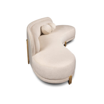 A modern, beige, curved sofa with a unique, semi-circular design. The sofa has a smooth fabric finish and is supported by gold-toned metal legs. There is a matching cylindrical bolster pillow resting on the seat.