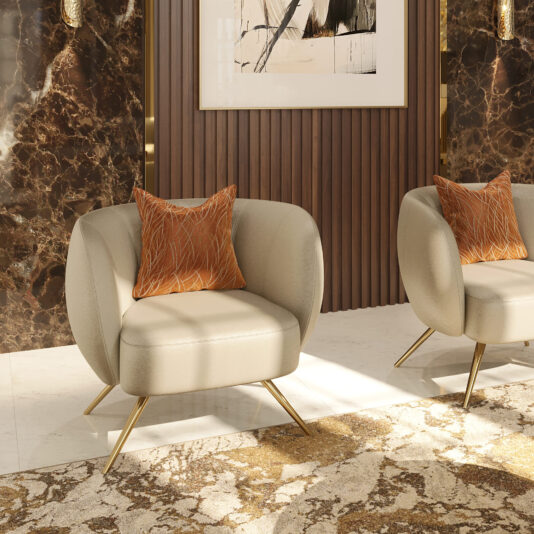 A modern living room features a Contemporary Leather Tub Armchair paired with beige armchairs with gold legs, each adorned with an orange patterned cushion. The backdrop showcases dark marble walls, wooden paneling, and a large abstract artwork. Sunlight brightens the space, highlighting a plush, earth-toned carpet.
