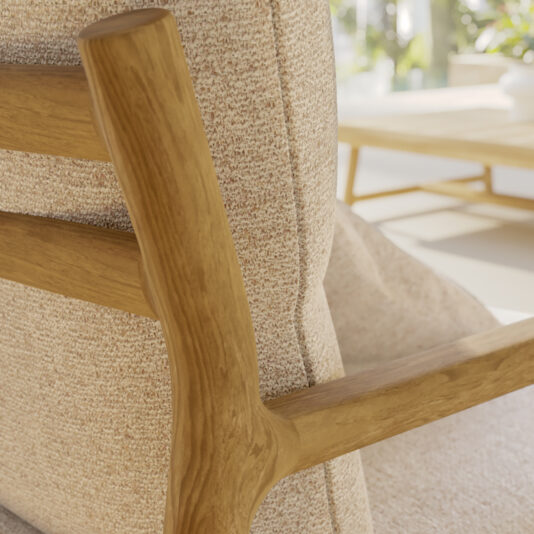 Close-up of a wooden armrest on a beige upholstered Contemporary Outdoor Deep Teak Armchair. The background is slightly blurred, showing a sunlit room with a coffee table and a hint of greenery outside the window.