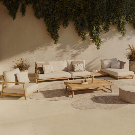 A serene outdoor seating area features the Contemporary Outdoor Teak Garden Set, which includes a sofa, chairs, and a chaise lounge with cushions. A wooden coffee table is centered on a large rug, with lush greenery hanging overhead to provide shade and a natural touch to the space.
