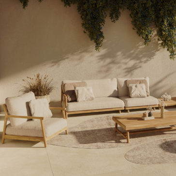 Contemporary Outdoor Teak Garden Set An outdoor seating area features the Contemporary Outdoor Teak Garden Set, which includes a beige sofa, matching armchair, and wooden coffee table. Light-colored cushions enhance the furniture, while potted plants and greenery hanging overhead cast soft shadows on the ground.