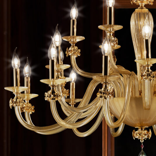 A close-up of the Hand Blown Glass Chandelier With Flowers showcases its ornate design, featuring multiple candle-like light bulbs. The chandelier includes intricate detailing with curved arms adorned with flowers and various decorative elements, all set against a dark background that accentuates its warm glow.