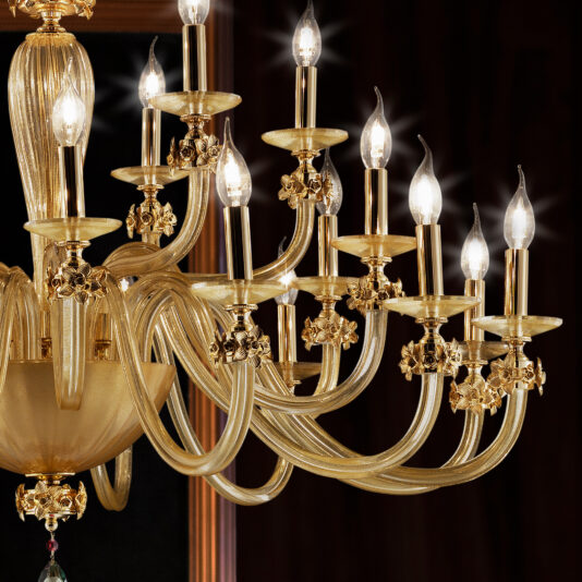 A close-up view of the Hand Blown Glass Chandelier With Flowers reveals nine lit, candle-shaped bulbs nestled in elegant golden holders. The chandelier showcases intricately designed arms adorned with delicate floral accents and a central bowl finished in luxurious, polished gold, set against a dark background.