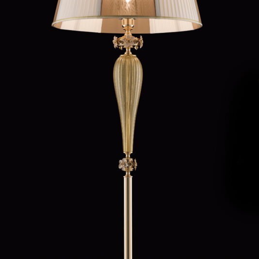 Hand Blown Glass Floor Lamp With Flowers Introducing the Hand Blown Glass Floor Lamp With Flowers: this elegant piece features a gold-colored, ornate design and a pleated lampshade adorned with floral elements. The black background accentuates its intricate beauty, from the decorative base to the detailed, vertically ribbed stem that gracefully narrows at the bottom.