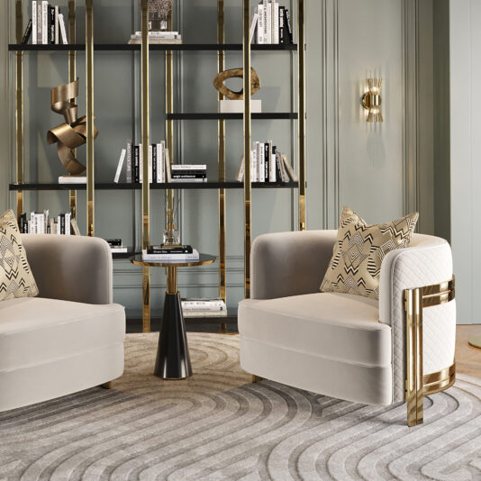 A stylish seating area showcases two Modern Curved Armchairs in light gray, each adorned with geometric-patterned pillows. These armchairs flank a small black side table topped with a golden figurine. A modern bookshelf filled with books and decorative items stands against a pastel green wall, which is decorated with a wall sconce.