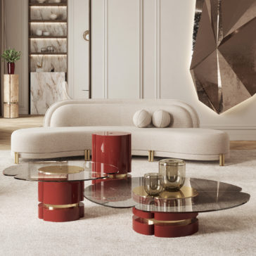 Modern Lacquered Coffee Table Set A modern living room showcases a curved white sofa with two round cushions, a beige rug, and the Modern Lacquered Coffee Table Set featuring glass and red cylindrical pieces. A large geometric wall sculpture and a plant enhance the background, creating a stylish and elegant atmosphere.