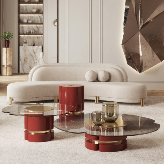 A modern living room showcases a curved white sofa with two round cushions, a beige rug, and the Modern Lacquered Coffee Table Set featuring glass and red cylindrical pieces. A large geometric wall sculpture and a plant enhance the background, creating a stylish and elegant atmosphere.
