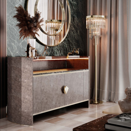 A luxurious interior features a gray marble sideboard with a geometric handle, adorned with a mirror, vase containing dried pampas grass, and gold accents. Adjacent to it stands the Modern Veneer 2 Door Cabinet, enhancing the space's functionality. A crystal floor lamp to the right casts light reflections on the dark marble wall.