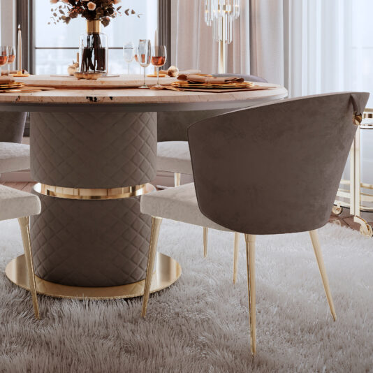 Elegant dining room showcasing a round table with a quilted base and gold accents, surrounded by Two-Tone Contemporary Dining Chairs featuring grey upholstery and gold legs. The table is set with sophisticated dinnerware, glasses, and a stunning floral centerpiece. Plush grey carpeting enhances the overall luxurious ambiance of the room.