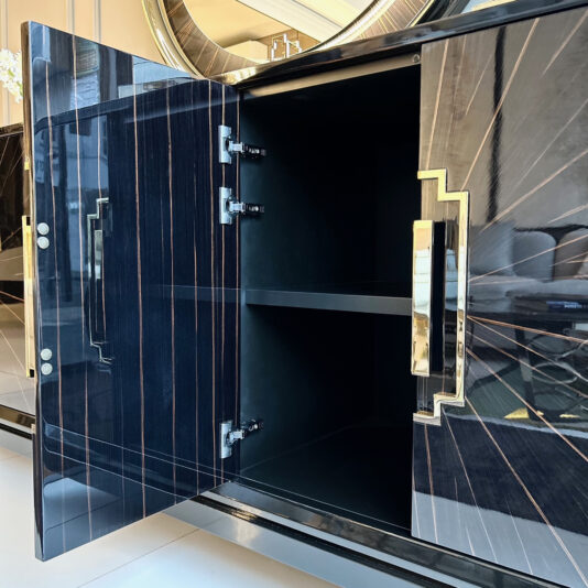 The High End Veneer Art Deco Style Sideboard is a black cabinet adorned with intricate gold and silver accents. Its open doors reveal an empty inner shelf, showcasing the sleek, glossy finish of its high-end veneer. This piece perfectly complements an elegant modern interior design setup.