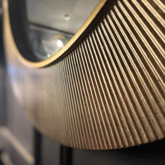 Modern Ribbed Round Mirror Close-up of the edge of the Modern Ribbed Round Mirror, showcasing its textured, ribbed frame in a metallic gold finish. The background is blurred, emphasizing the intricate detail and texture of the mirror frame.