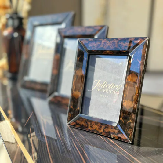 Three photo frames with a glossy, dark wood finish are displayed on a reflective tabletop. Branded 