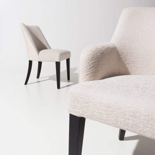 High End Leather Backed Carver Dining Chair Two High End Leather Backed Carver Dining Chairs in beige, featuring dark wooden legs, are positioned in a minimalist white room. One chair is prominently featured in the foreground, partially out of focus, while the other is fully visible in the background, highlighting their contemporary design.