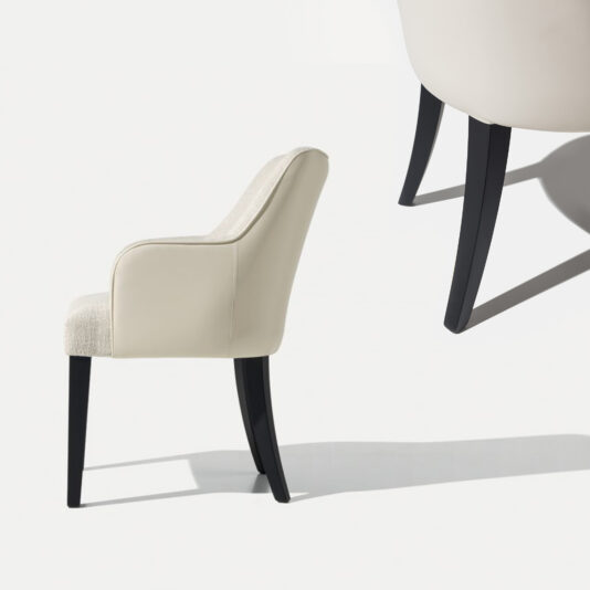 High End Leather Backed Carver Dining Chair A modern, armless High End Leather Backed Carver Dining Chair with black angled legs and a light beige upholstered seat and backrest is seen from the side, casting a shadow on a white background. An enlarged partial section of the chair's back and legs is displayed at the top right.