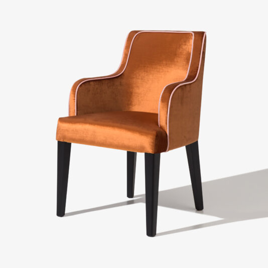 High End Occasional Chair With Piping Detail Introducing the High End Occasional Chair With Piping Detail: a stylish piece that exudes elegance with its orange velvet upholstery and contrasting white piping outlining the edges. This chair boasts a high back, gently curved armrests, and dark wooden legs, all set against a plain white backdrop to highlight its sophisticated design.