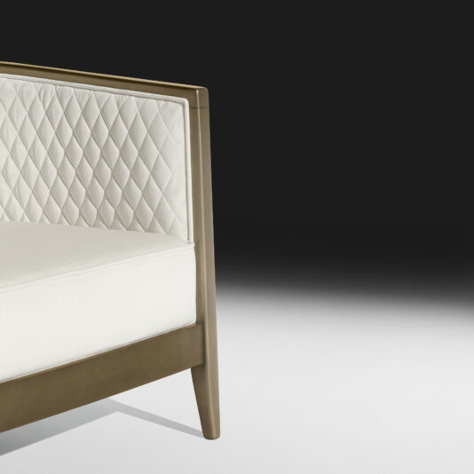 A close-up view of the High End Quilted Velvet Tub Chair showcases its modern design, featuring a white leather backrest and seat cushion, complemented by sleek wooden armrests and legs. The background transitions from black at the top to white at the bottom.