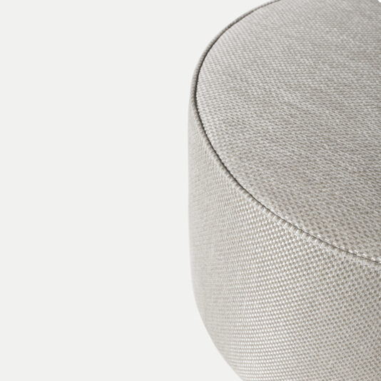 Close-up of the High End Round Pouffe, revealing its light gray textured fabric with an intricate weave and slightly curved surface. The subtle gradient and fine detailing of the material are highlighted, emphasizing its elegant and smooth finish—ideal for this high-end piece.