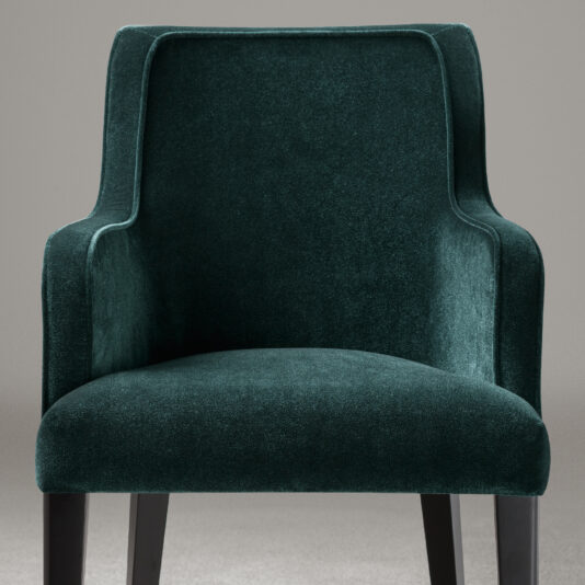 A luxurious High End Occasional Velvet Armchair in dark green features curved armrests and a high backrest. The chair, with its black wooden legs, is set against a plain grey background. The soft velvet fabric enhances its elegant and comfortable appearance.