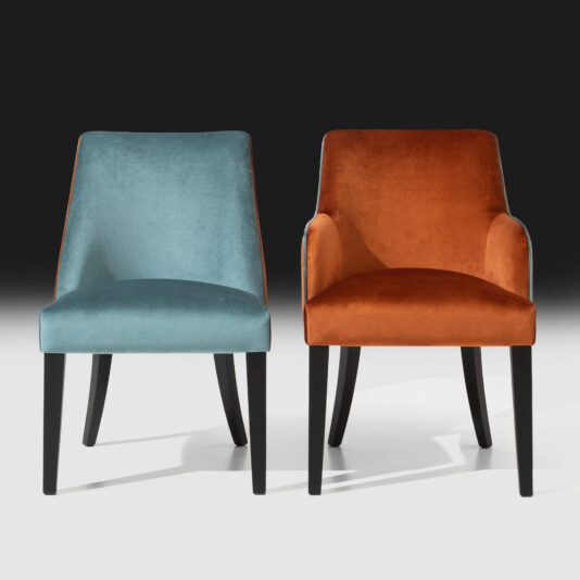 Two **High End Velvet Dining Chairs With Piping** and black wooden legs are placed side by side against a gradient background. The chair on the left is covered in teal fabric, while the one on the right features burnt orange fabric with elegant piping. Both chairs have a contemporary design with gently curved backs.