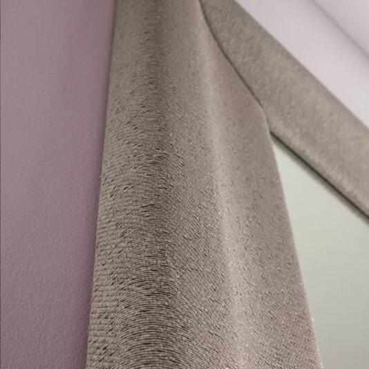 Close-up of the Large Contemporary Fabric Floor Mirror, featuring a textured beige frame, mounted on a light purple wall. The frame's subtle pattern adds an elegant touch to the decor. The angle of the shot highlights the intricate details of the frame and the corner of the mirror.