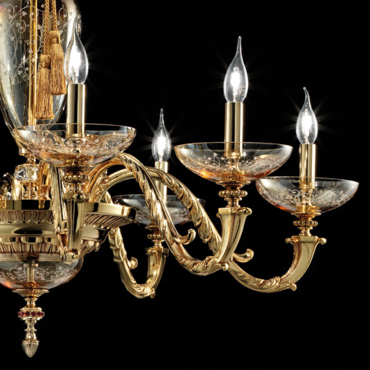 Amber Hand Blown Glass Chandelier The Amber Hand Blown Glass Chandelier is a luxurious and ornate lighting fixture featuring five candle-shaped light bulbs, each set in decorative hand-blown amber glass holders. Its intricate design showcases elegant gold curves and detailed craftsmanship, all beautifully contrasted against a black background.