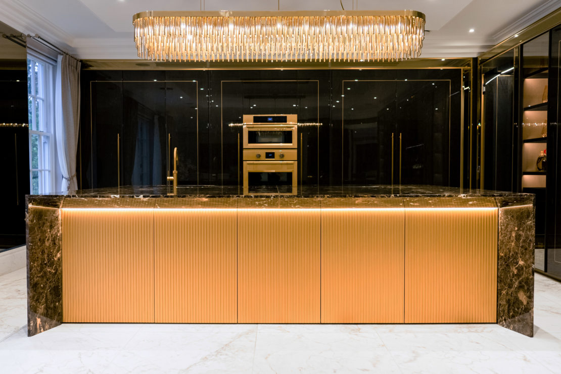 Stunning art deco influenced luxury kitchen designed by Juliettes Interiors with statement modern chandelier, rich marble topped centre island with under bench lighting