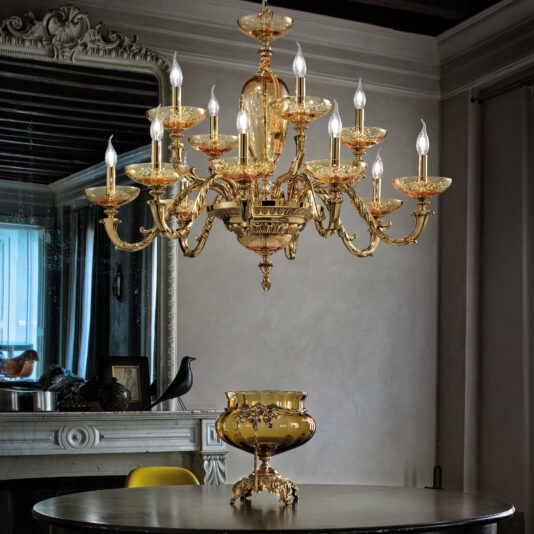 Large Hand Blown Amber Glass Chandelier A luxurious dining room featuring a Large Hand Blown Amber Glass Chandelier suspended above a round black table, which holds a decorative gold vase. In the background, a large framed mirror reflects part of the room, and a mantel adorned with decorative items is visible.