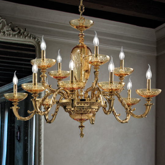 A luxurious, ornate Large Hand Blown Amber Glass Chandelier with twelve candle-like lights arranged in two tiers adorns the elegant room. Each light is complemented by large hand-blown amber glass shades. The chandelier hangs elegantly while a decorative mirror on the left wall and wooden beams on the ceiling complete the sophisticated ambiance.