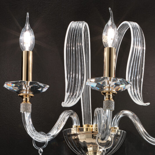 Triple Leaf Wall Light With Swarovski® Crystals A close-up of the elegant Triple Leaf Wall Light With Swarovski® Crystals, showcasing two candle-shaped bulbs. The fixture features gold accents and a sleek, reflective flowing clear glass design, set against a dark background.