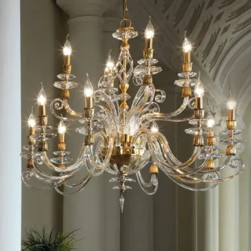 Candle Style Swarovski® Crystal Chandelier The **Candle Style Swarovski® Crystal Chandelier** is a grand, ornate piece featuring multiple tiers of curved, clear glass arms holding candle-like light bulbs with golden accents. The chandelier stands out beautifully against a backdrop of white, columned arches and an intricately patterned ceiling.