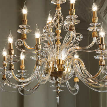 Candle Style Swarovski® Crystal Chandelier The Candle Style Swarovski® Crystal Chandelier radiates a warm glow with its crystal and gold elements. The elaborate design includes multiple curved arms, each adorned with a single candle-shaped bulb. This chandelier exudes elegance through its intricate details and sparkling appearance.