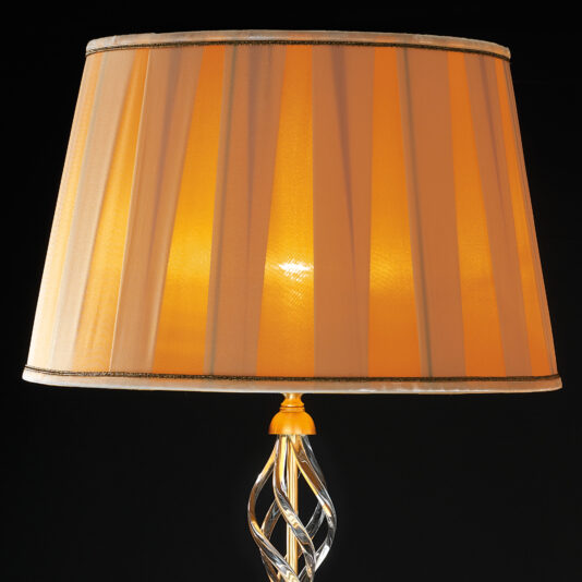 A lit Classic Style Twisted Table Lamp features a warm, orange lampshade adorned with subtle vertical stripes and an elegantly twisted base design. The dark background enhances the inviting glow of this sophisticated and timeless piece.