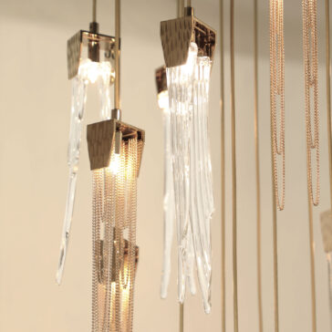 Contemporary Chain And Glass Stairwell Chandelier The Contemporary Chain And Glass Stairwell Chandelier features modern vertical glass elements and gold chains hanging from the ceiling. It emits a soft, warm glow that creates an elegant and sophisticated ambiance, capturing a minimalist aesthetic.